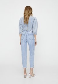 Chaqueta de mezclilla azul clara con mangas abullonadas y un corte corto, combinada con jeans azul claros ajustados con puños doblados y bolsillos traseros.