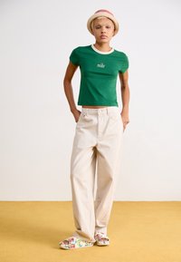 T-shirt vert ajusté avec col blanc portant le logo "nike", associé à un pantalon large crème et des chaussures ouvertes à motif floral.