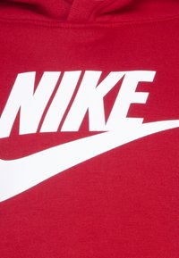 Piros kapucnis pulóver nagy fehér Nike logóval és pipa emblémával. Az anyag textúrált, kapucnival és bordás mandzsettákkal rendelkezik. Egyszerű dizájn minta nélkül.