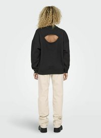 Svart hoodies med en utskärning på baksidan, tillsammans med ljusbeiga byxor. Mjuk tyg, avslappnad passform och ribbade ärmslut. Svarta platåskor.