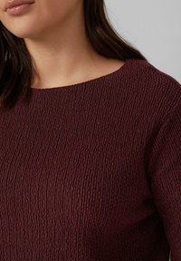 Burgunderfarbener, strukturierter Oberteil mit geripptem Design, das einen weiten Ausschnitt und kurze Ärmel aufweist. Der Stoff wirkt weich mit einem leichten Schimmer.