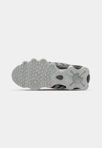 Sports shoe with a predominantly black upper, textured material, and a white rubber outsole featuring a patterned grip design and orange accents.