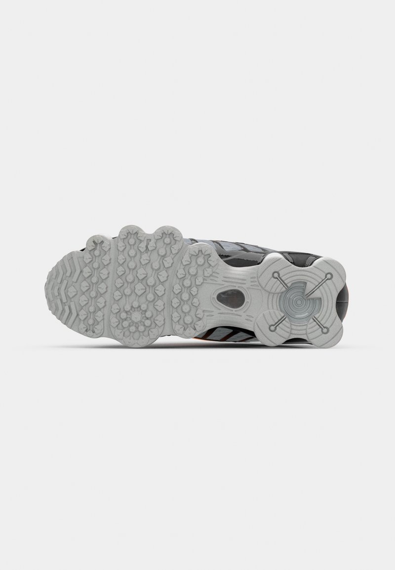 Chaussure de sport avec un upper principalement noir, en matériau texturé, et une semelle en caoutchouc blanche présentant un design de grip à motifs et des accents orange.