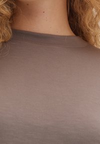 Camiseta marrón ajustada con cuello redondo, hecha de una tela suave y lisa. Presenta costuras sutiles a lo largo del escote y no tiene patrones ni detalles visibles.