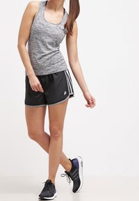 Débardeur de sport gris sans manches associé à un short noir avec des bandes latérales blanches. Le mannequin porte des chaussures de course noires.