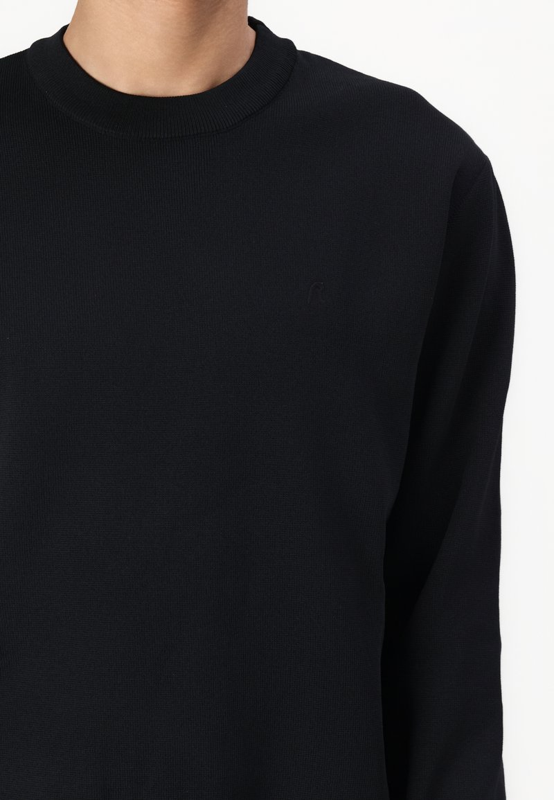 Maglione nero lavorato a maglia con scollo rotondo e texture a coste. Presenta un discreto dettaglio del logo sul petto. Design elegante e aderente. Maniche lunghe.