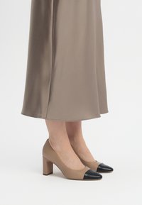 Beige korkokengät mustalla kärjellä, joissa on sileä pinta ja paksu korko, yhdistettynä ruskeaan satiinishortsiin.