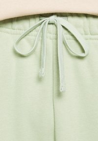 Joggers verde claro con una textura suave, que cuentan con un cierre de cordón y una tela lisa, mostrando costuras a lo largo de la cinturilla.