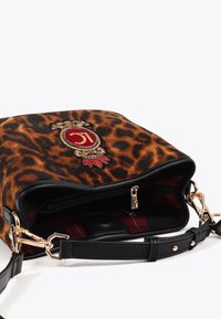 Torba s leopard uzorkom od mekanog materijala s crnim kožnim detaljima, zlatnim metalnim dijelovima, unutarnjim džepom i istaknutim izvezenim logom sprijeda.