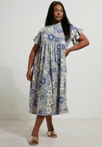 Niebieska sukienka w kwiatowy wzór z krótkimi falbanianymi rękawami, luźny krój, do kolan, wykonana z lekkiego materiału. W zestawieniu ze złotymi sandałami.