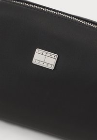 Juodas dirbtinės odos maišelis su sidabriniu užtrauktuku. Ypatybės: stačiakampis sidabrinis logotipo plakatas su užrašu "TOMMY JEANS". Lygus paviršius, minimalistinis dizainas.