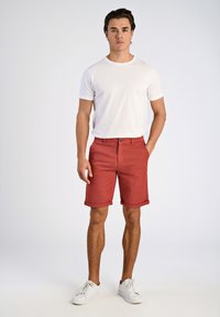 Shorts en coton rouge avec un devant plat, des poignets roulés et des poches latérales, associés à un t-shirt blanc à manches courtes et des baskets blanches.