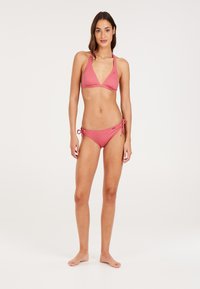 Bikini rosa a coste con top triangolare e slip regolabili con lacci laterali. Tessuto morbido, minimal hardware e design aderente.