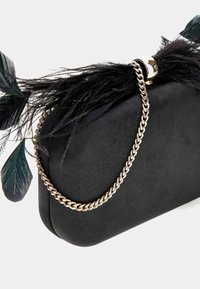 Juodas zomšinės odos delninukas su auksiniu grandininiu rankenėle, papuoštas juodais plunksnų akcentais ir teal spalva viršuje. Stačiakampio formos, su lygiu paviršiumi.