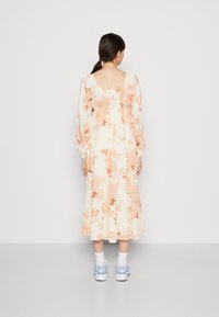 Kwiatowa długa sukienka z kwadratowym dekoltem, bufiastymi rękawami, w kremowym kolorze z brzoskwiniowymi kwiatami. Uzupełniona białymi skarpetkami i niebieskimi trampkami.