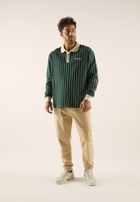Groen gestreepte lange mouw polo met een crèmekleurige kraag, gecombineerd met beige tapering pants en lichte sneakers.