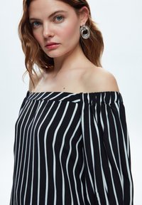 Off-the-shoulder top med sort og hvid lodret strib. Letvægtsstof med en samlet halsudskæring og lange, løse ærmer. Sølvfarvede hoop øreringe.