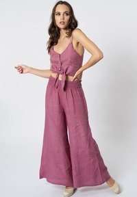 Completo a due pezzi in una tonalità di lavanda morbida e textured. La parte superiore presenta una chiusura a bottoni e un nodo in vita. I pantaloni a gamba larga hanno una vita elasticizzata.