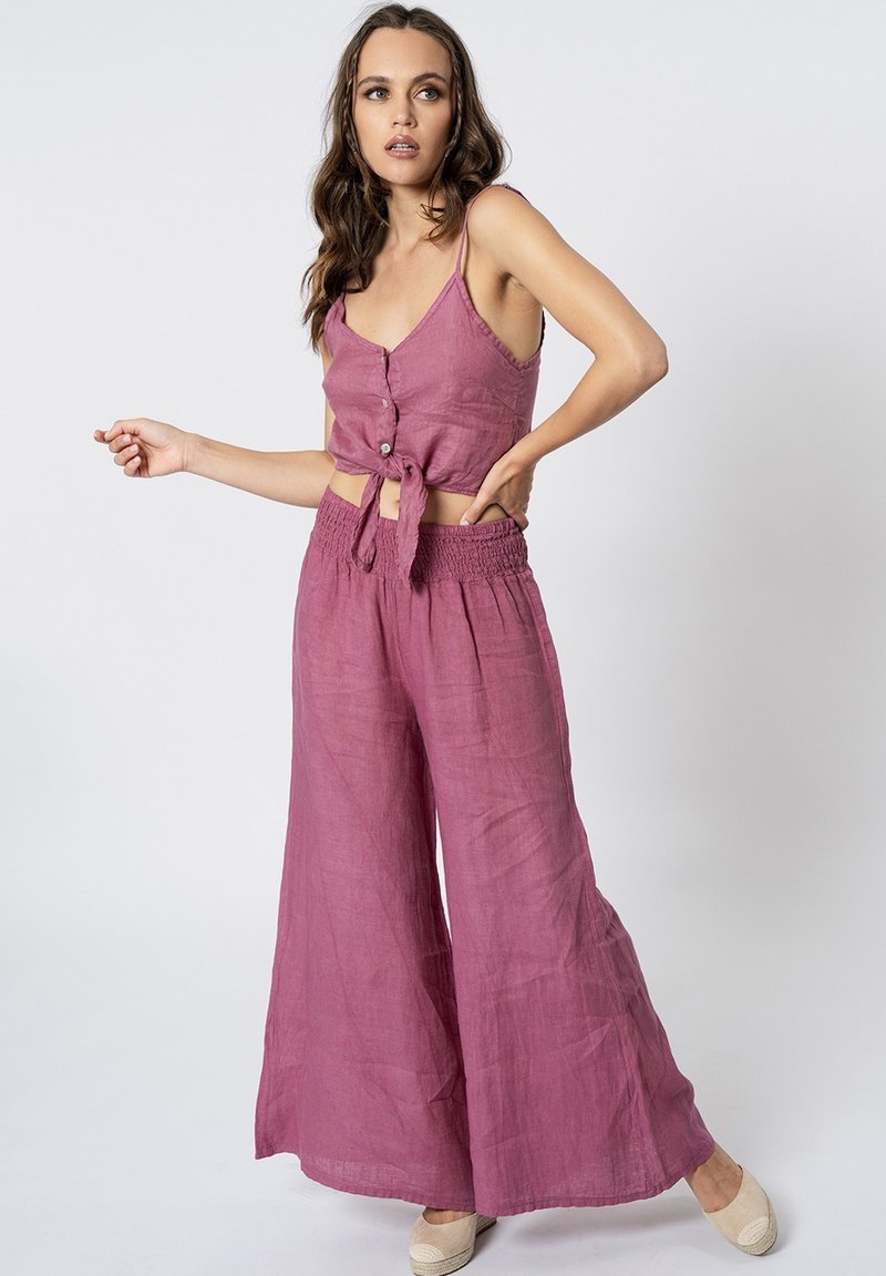 Completo a due pezzi in una tonalità di lavanda morbida e textured. La parte superiore presenta una chiusura a bottoni e un nodo in vita. I pantaloni a gamba larga hanno una vita elasticizzata.