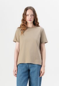 Kaki T-skjorte med korte ermer og rund hals, laget av mykt stoff. Sammen med høytlivede blå denimjeans. Enkel, avslappet design.