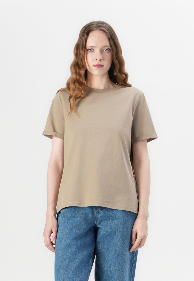 Kaki T-skjorte med korte ermer og rund hals, laget av mykt stoff. Sammen med høytlivede blå denimjeans. Enkel, avslappet design.
