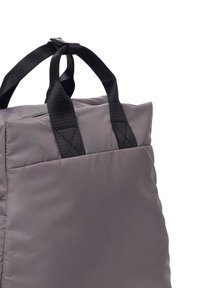 Bolsa acolchada gris con correas de nailon negras. Presenta una forma rectangular, textura suave y un cierre con cremallera en el lateral.