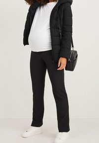 Chaleco acolchado negro con capucha, camiseta blanca ajustada, leggins negros y zapatillas blancas. Bolso negro portátil con correa.