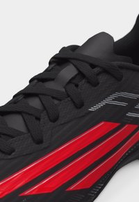 Κοντινό πλάνο μαύρου αθλητικού παπουτσιού με υφασμένες κορδόνια και τρεις έντονες κόκκινες ρίγες στο πλάι για σχεδιασμό.