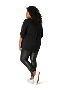 Zwarte blouse met lange mouwen en een vloeiende pasvorm, gecombineerd met strakke zwarte leren leggings en witte sneakers met een gestructureerde zool.