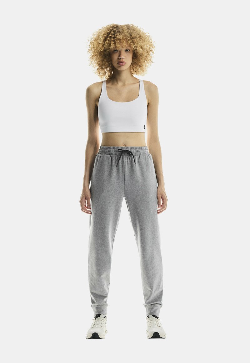 Pantaloni de trening gri cu talie elastică și șnur, asortați cu un top scurt alb. Ținuta are un fit casual și o textură netedă.