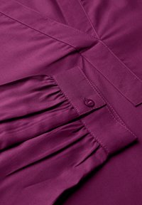 Blusa prugna con dettaglio plissettato vicino alla chiusura dei bottoni. Tessuto morbido, design sartoriale, con cuciture ordinate lungo i bordi.