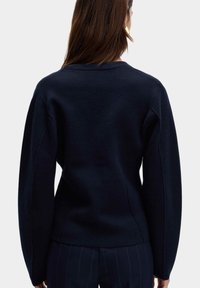 Granatowa bluza z okrągłym dekoltem, długimi rękawami i teksturowanym wykończeniem. Ma ergonomiczną sylwetkę i widoczne detale szwów.