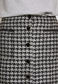 Sukně s pepitovým vzorem v černé a bílé barvě, zdobená zlatými knoflíky a texturovanou tkaninou s přiléhavým pasem.