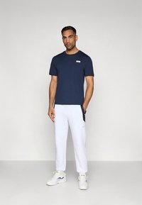 Μπλε ναυτικό βαμβακερό t-shirt με στρογγυλή λαιμόκοψη και μικρό λευκό λογότυπο στο στήθος, σε συνδυασμό με λευκές φόρμες με πλαϊνές τσέπες.