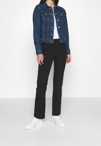 Jeansjacka i mörkblå med framfickor och silverknappar, kombinerad med svarta slim fit-byxor och vita sneakers. Enkel och skräddarsydd design.