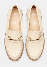 Mocassini in pelle beige con finitura liscia, caratterizzati da un accento dorato sulla parte anteriore e una soletta beige imbottita. Suola in gomma.