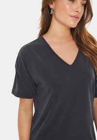Mörkgrå T-shirt med kort ärm och V-ringning, tillverkad av ett slätt, lätt material med subtil textur. Har ren sömnad och en avslappnad passform.