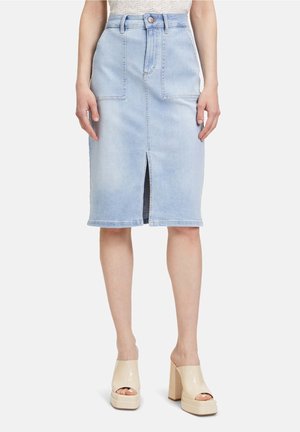 Falda azul claro de mezclilla hasta la rodilla con abertura frontal y bolsillos, combinada con tacones abiertos beige de plataforma.