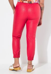 Rode, glanzende synthetische legging met een elastische tailleband en gathered manchetten, gecombineerd met een witte platform sandaal.