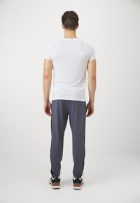 Hvid kortærmet T-shirt parret med grå sweatpants med sorte sidelister, båret med sneakers, set fra ryggen.