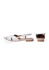 Białe sandały na obcasie typu slingback z noskiem w kształcie szpica i wyciętym wzorem, z płaskim, brązowym obcasem i regulowanym paskiem przy kostce. Gładka skóra.