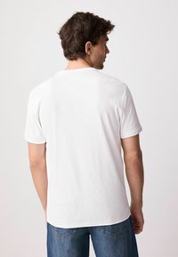 Tricou alb cu maneci scurte, cu o textură ribandă și guler rotund, asortat cu blugi din denim albastru. Fără modele notabile sau accesorii.