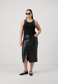 Top in cotone nero a costine con rifiniture bianche a scallop, abbinato a una gonna midi in pelle nera con una spacco laterale. Completa il look un paio di ballerine nere.