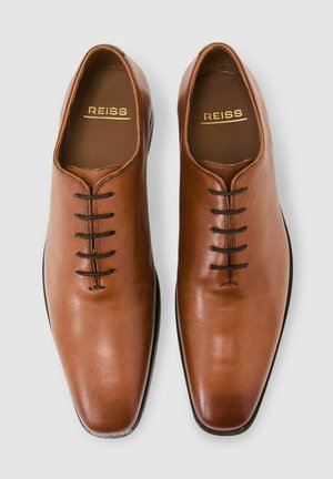 Pantofi maro deschis din piele cu un design elegant și ascuțit. Au șase găuri negre pentru șireturi, o suprafață netedă și un logo subtil REISS imprimat pe interior.