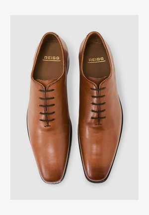 Pantofi maro deschis din piele cu un design elegant și ascuțit. Au șase găuri negre pentru șireturi, o suprafață netedă și un logo subtil REISS imprimat pe interior.