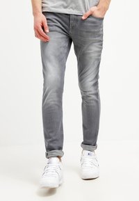 Vaqueros ajustados gris deslavado con un ligero toque de elasticidad, diseño de cinco bolsillos y puños remangados, combinados con zapatillas blancas.