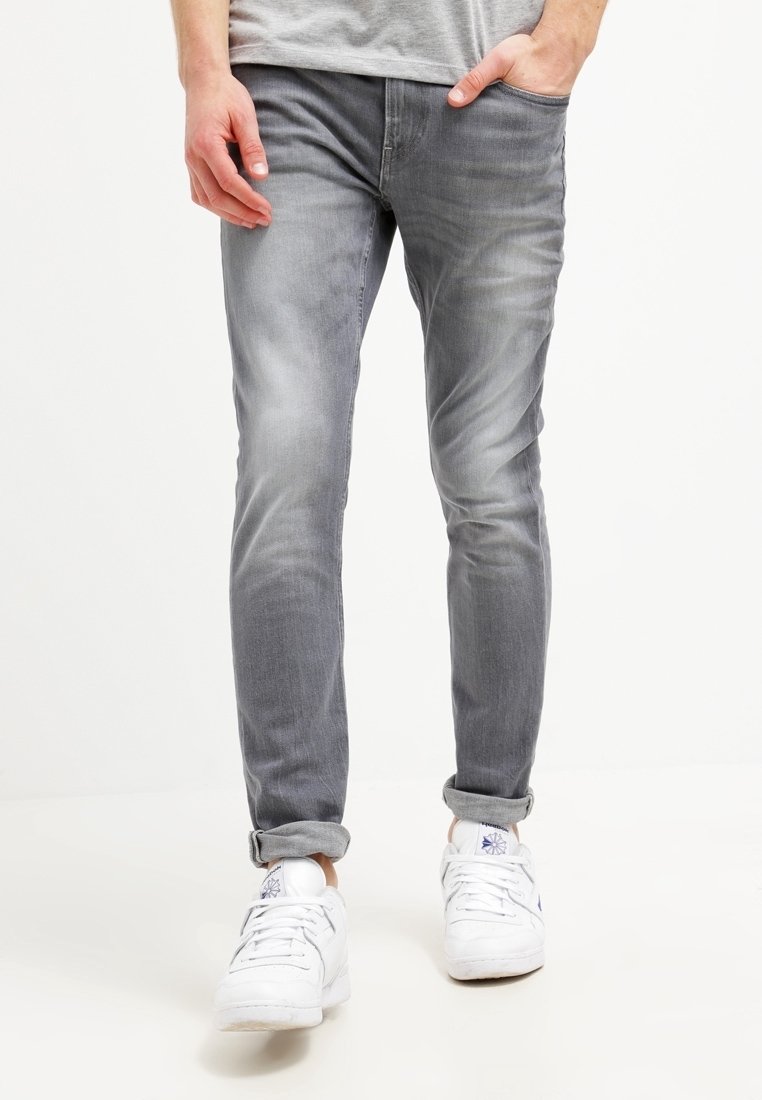 Vaqueros ajustados gris deslavado con un ligero toque de elasticidad, diseño de cinco bolsillos y puños remangados, combinados con zapatillas blancas.