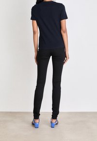 Camiseta de manga corta azul marino combinada con pantalones ajustados negros y zapatos de tacón azul, vista desde la espalda, mostrando una silueta elegante.