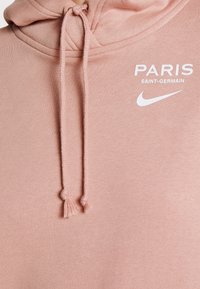 Felpa rosa chiaro con cordini, caratterizzata da testo bianco "PARIS SAINT-GERMAIN" e logo Nike a forma di baffo sul petto.