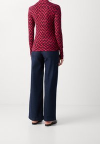 Top a maniche lunghe rosso e nero con motivo abbinato a pantaloni in jeans scuri a gamba larga. Tessuto testurizzato, vestibilità classica e sandali a pianta piatta minimalisti.